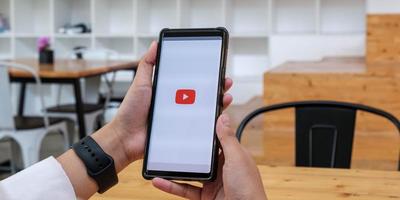 thailand - 20. januar 2021 - frau, die smartphone mit videoservice youtube auf dem bildschirm hält. foto