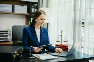 weiblich Richter im ein Gerichtssaal das Hammer, Arbeiten mit Clever Telefon und Laptop und Digital Tablette Computer auf Holz Tabelle foto