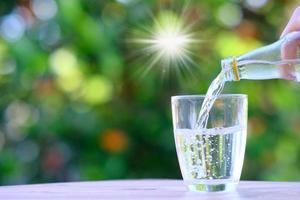 Hand, die Wasser in eine Glastasse mit einem Bokeh-Naturhintergrund gießt foto