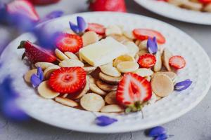 Pfannkuchen-Müsli, trendiges Essen. Mini-Getreidepfannkuchen mit Butter, Honig und Erdbeeren.