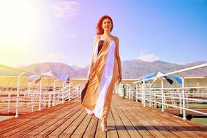 Rothaariges Mädchen posiert in einem flatternden Kleid auf dem Pier.