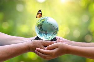 Erwachsene schicken Babys die Welt. Konzepttag Erde rette die Welt rette die Umwelt Die Welt liegt im Gras des grünen Bokeh-Hintergrunds