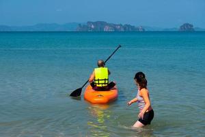 Asiatischer Senior-Vater, der im Sommerurlaub Paddleboard oder Sup mit kleiner Tochter am blauen Meer spielt. Familie zusammen Konzept