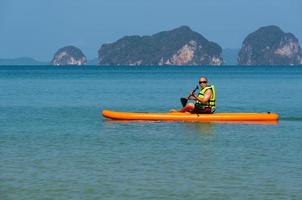 Älterer asiatischer Mann, der während der Sommerferien Paddle-Board im blauen Meer spielt foto
