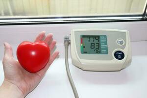Foto tragbar Blut Druck Monitor - - gedreht auf Gerät mit Indikatoren auf das Bildschirm und ein Gummi Hand Trainer im das gestalten von ein Herz im ein Frau Hand
