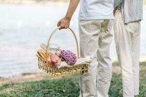 Paar Gehen im Garten mit Picknick Korb. im Liebe Paar ist genießen Picknick Zeit im Park draußen foto