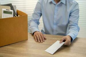 Senden Rücktritt Brief zu Boss und halten Zeug zurücktreten drücken oder Tragen Karton Box durch Schreibtisch im Büro foto