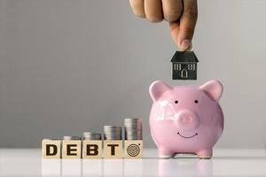 Konzept der Schulden und finanziellen Ziele.coin auf gestapelten Holzblöcken mit der Bezeichnung Schulden und Hände, die Hausmodell in rosa Schweinesparungen halten. foto
