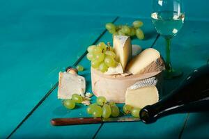 Käse, Trauben und Wein auf hölzern cyan Oberfläche. foto