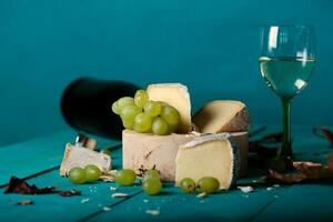 Käse, Trauben und Wein auf hölzern cyan Oberfläche. foto