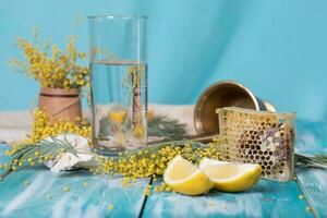 Glas von Wasser, Mimose Blumen, Bienenwabe und Stücke von Zitrone foto
