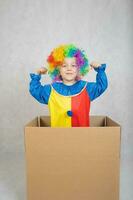 Junge von fünf Jahre gekleidet im das Kostüm von ein Clown bleibt im ein Karton Papier Kasten. foto