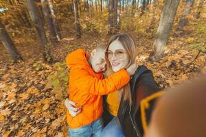 Sohn und Mutter sind nehmen Selfie auf Kamera im Herbst Park. Single Elternteil, Freizeit und fallen Jahreszeit Konzept. foto