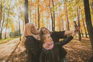 drei Generationen von Frauen und Hund Gefühl Spaß aussehen beim Kamera posieren zum Selbstporträt Bild zusammen, komisch aufgeregt Kind, Mama und Oma haben Spaß genießen Wochenende nehmen Selfie auf Gadget im Herbst foto