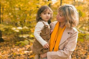 jung Mutter mit ihr wenig Tochter im ein Herbst Park. fallen Jahreszeit, Erziehung und Kinder Konzept. foto