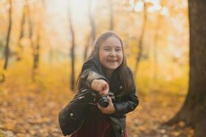 ein wenig Mädchen nehmen ein Foto mit alt retro Kamera im Herbst Natur. Freizeit und Hobby Konzept.