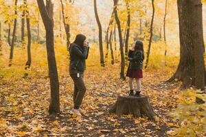 Mutter nehmen Bild ihr charismatisch Tochter auf retro Kamera im Herbst Park. Hobbys und Freizeit Konzept. foto