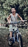 ein Junge mit lustigem Gesicht, der sein altes rustikales Fahrrad fährt. ein kleiner Junge fährt mit seinem alten Fahrrad im Hinterhof und macht ein lustiges Gesicht. foto