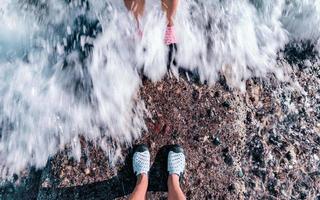 Paar steht zusammen am steinernen Ufer. Füße des Paares bedeckt von Wasserwelle am Meer. foto