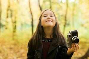 Kind Mädchen mit ein altmodisch Kamera im Herbst Natur. Fotograf, fallen Jahreszeit und Freizeit Konzept. foto