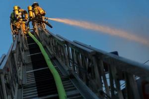 Feuerwehrleute klettern Leiter gegen Bau und Löschen eines Brandes foto
