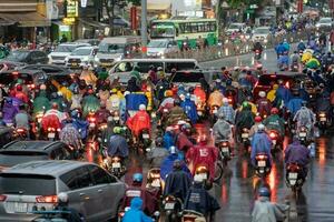 ho Chi Minh, viet nam - - 24 April 2023 Vietnamesisch Menschen tragen Helm und Regenjacke Reiten Motorrad im schwer Regen und der Verkehr Marmelade. foto