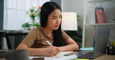 ung asiatisch Frau Arbeiten mit ein Laptop und Schreiben auf Papier auf ein Schreibtisch foto