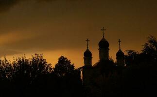 das Silhouette von das Kuppeln von ein orthodox Christian Kirche im Rumänien gegen das Hintergrund von das rot Himmel. Vertrauen oder Religion Konzept Foto