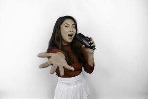porträt einer sorglosen asiatischen frau, die spaß beim karaoke hat und im mikrofon singt, während sie über weißem hintergrund steht foto