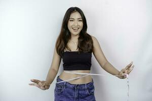 Gewicht Verlust, schlank Körper, gesund Lebensstil Konzept. passen Fitness asiatisch Mädchen Messung ihr Taille mit Messung Band, isoliert durch Weiß Hintergrund foto