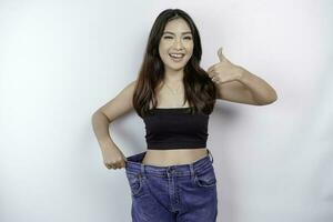 Diät und Gewicht Verlust Konzept. ein jung asiatisch Frau im übergroß Jeans isoliert auf ein Weiß Hintergrund. foto