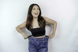 Diät und Gewicht Verlust Konzept. ein jung asiatisch Frau im übergroß Jeans isoliert auf ein Weiß Hintergrund. foto