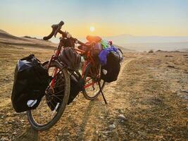 geladen mit Taschen rot Fahrrad steht auf Seite von Straße umgeben durch Berge im Landschaft von Vashlovani National Park. Fahrrad Touring Urlaub im Georgia foto