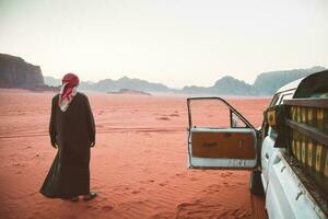 beduinenfahrer reiseveranstalter stehen nach sonnenuntergang in der wüste wadi rum mit einem fahrzeug mit allradantrieb. Besuchen Sie Jordan Tours im berühmten Wadi-Rum-Reservat im Nahen Osten foto