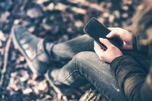 jung kaukasisch Frauen Tippen auf ihr Telefon im das Wald. foto