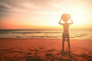 jung Mann mit Surfbrett auf Sonnenuntergang Sommer- tropisch Strand Hintergrund. foto