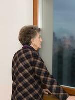 alt Frau von 80 Jahre alt bleibt schließen zu das Fenster foto