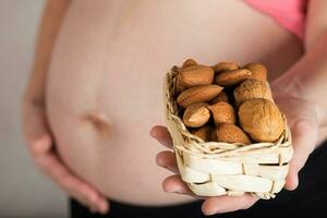 jung schwanger Frau hält gewebte Mini Korb voll von Nüsse. foto