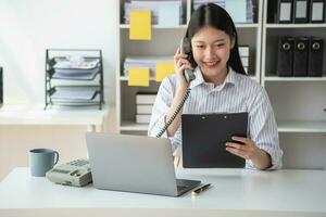 asiatisch Geschäftsfrau reden auf das Telefon Arbeiten im modern Büro Plaudern mit Kunden zum ein Neu Weg von tun Geschäft im das Büro. foto