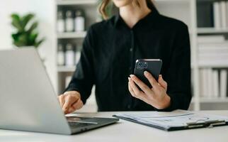 Hände von Frau mit Handy, Mobiltelefon Telefon im modern Büro mit Laptop und Digital Tablette beim Büro foto