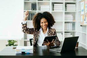 afrikanisch Geschäft Frau sind Erfreut und glücklich mit das Arbeit Sie tun auf ihr Tablette, Laptop und nehmen Anmerkungen beim das Büro. foto