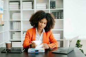 jung afrikanisch Frau Tippen auf Tablette und Laptop während Sitzung beim das Arbeiten schwarz Tabelle Büro foto