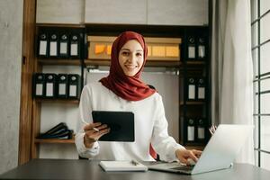 jung Arabisch weiblich Unternehmer tragen ein Hijab Arbeiten online mit ein Laptop beim Büro foto