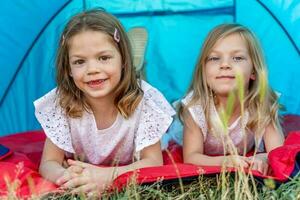 Porträt von zwei blond und ziemlich Schwestern Lügen Nieder im ein Blau Camping Zelt foto