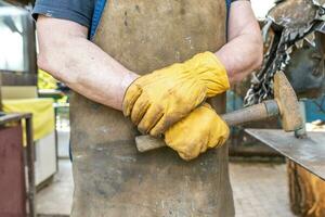 Detail von das Hände von ein Schmied. Eisen Arbeiter hält ein Hammer foto