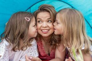 Porträt von süß blond Mama mit ihr Töchter Lügen Nieder im ein Blau Camping Zelt foto