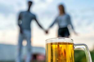 Nahansicht von ein Glas von Bier im Vorderseite von ein gemischtrassig Paar von Liebhaber verschwommen im das Hintergrund foto