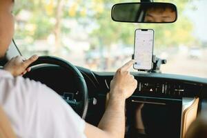 ein Mann fährt ein Auto mit ein Geographisches Positionierungs System Navigation System auf seine Handy, Mobiltelefon Telefon während Fahren, zu finden seine Ziel. Transport mit Technologie Konzept. foto