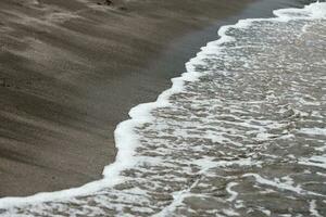 Welle auf das schwarz Sand Strand foto