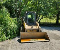 klein Gelb Traktor mit ein Eimer im das Park foto